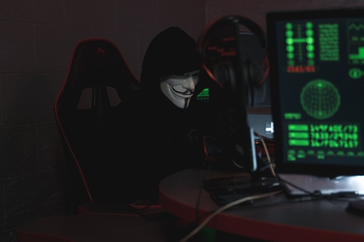 Anonymer Hacker mit einer Maske sitzt an einem Computer