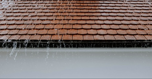 Regenwasser tropft an einer Dachrinne hinab 